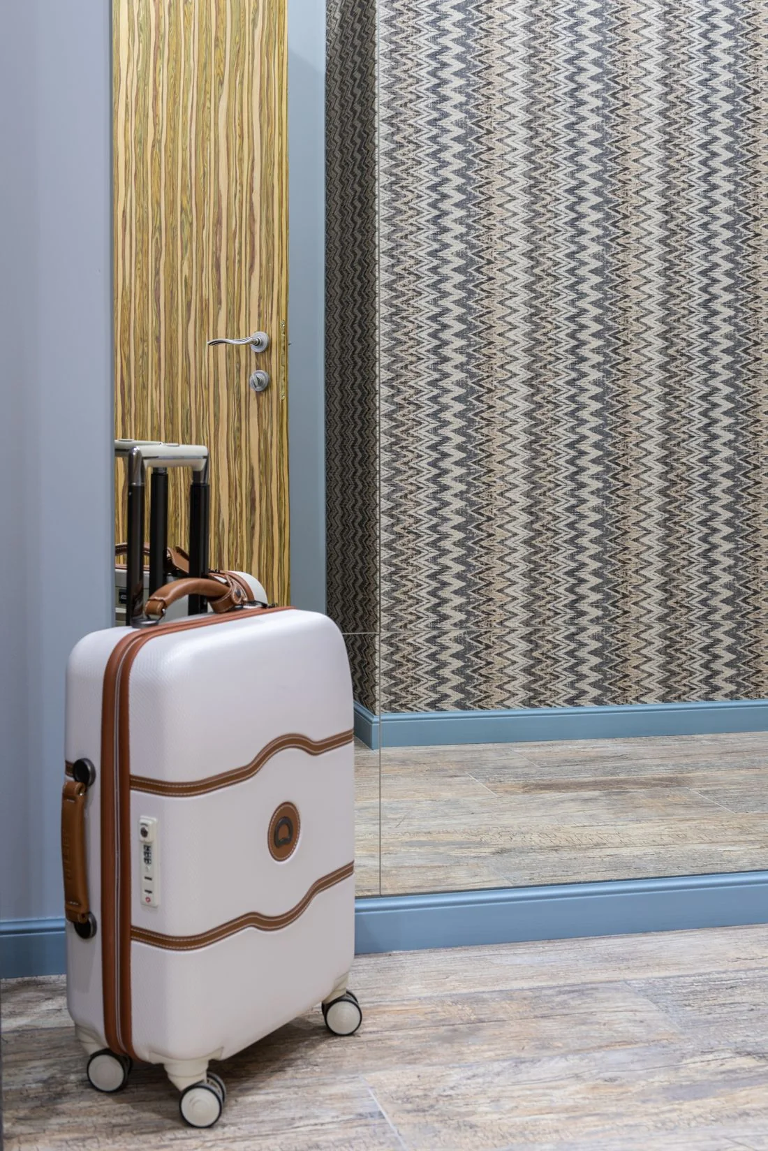 White suitcase beside a mirror in a modern hotel hallway