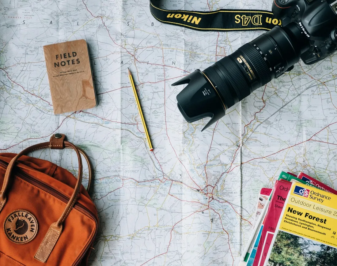 Travel notebook and camera beside a leather bag and map