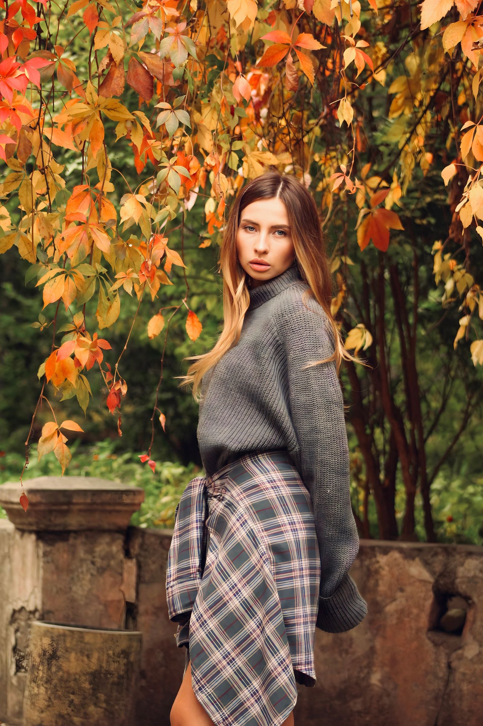 Woman wearing a sweater and plaid skirt among autumn leaves