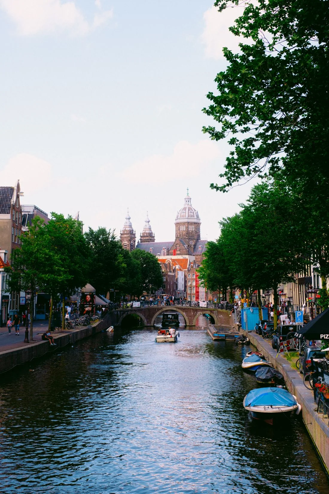 Amsterdam canal with a stone bridge, boats, trees and distant domes