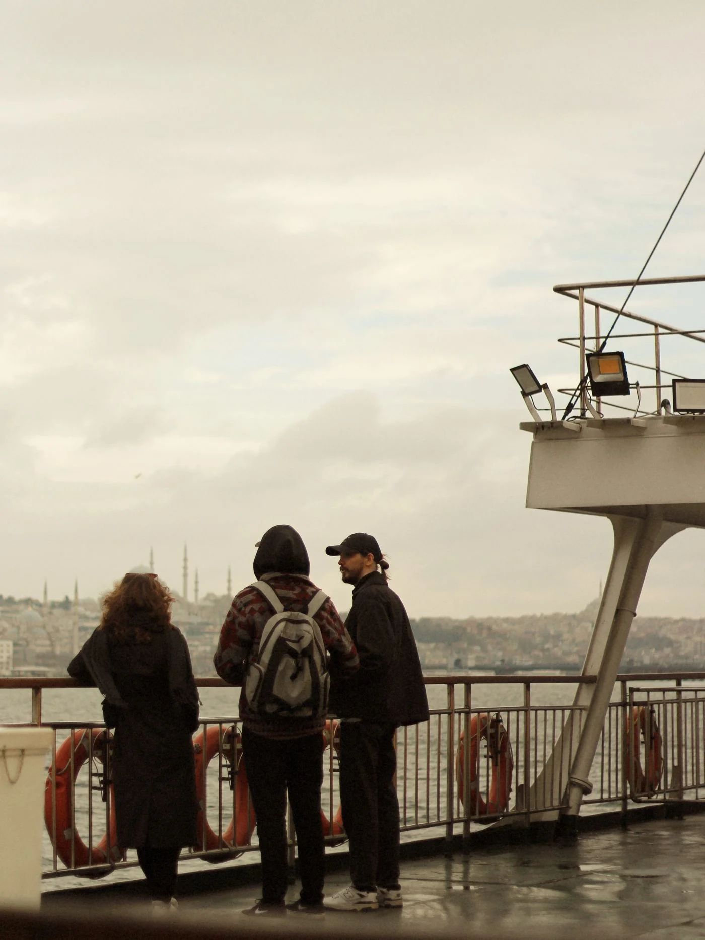 Three travellers looking across the water from a ferry deck