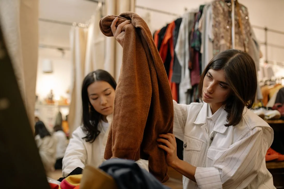 Two women examining a brown garment among racks in a clothing shop