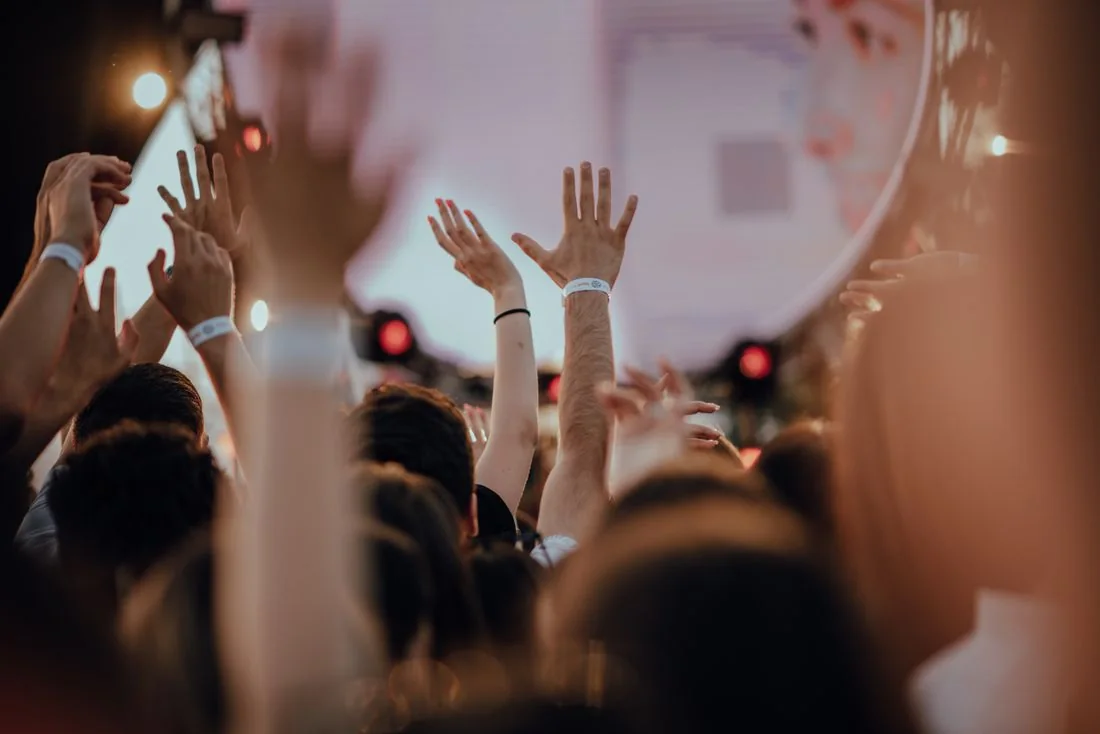Concert audience raising hands towards a lit performance space