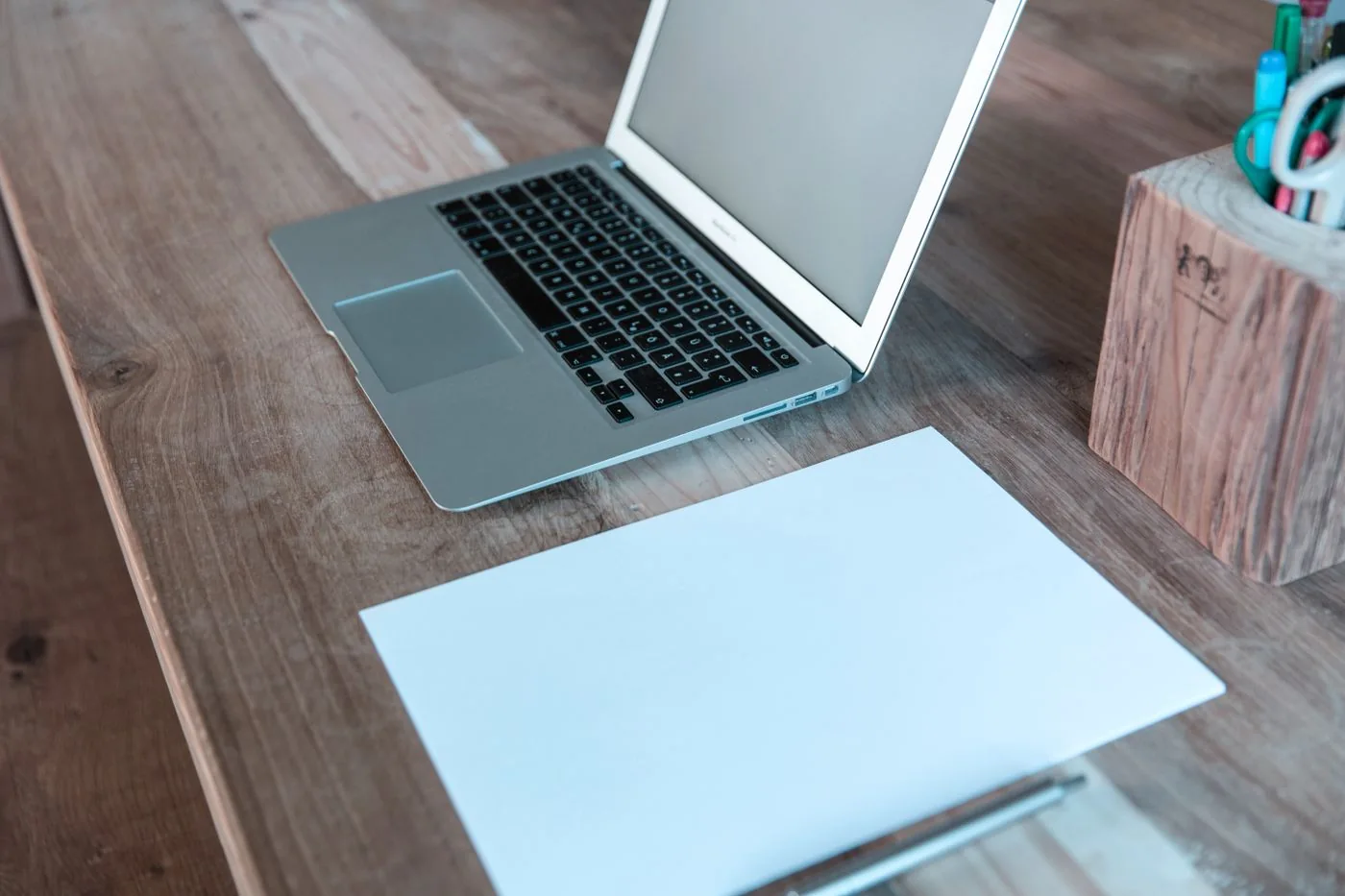 A laptop, paper, and pen on a wooden desk.