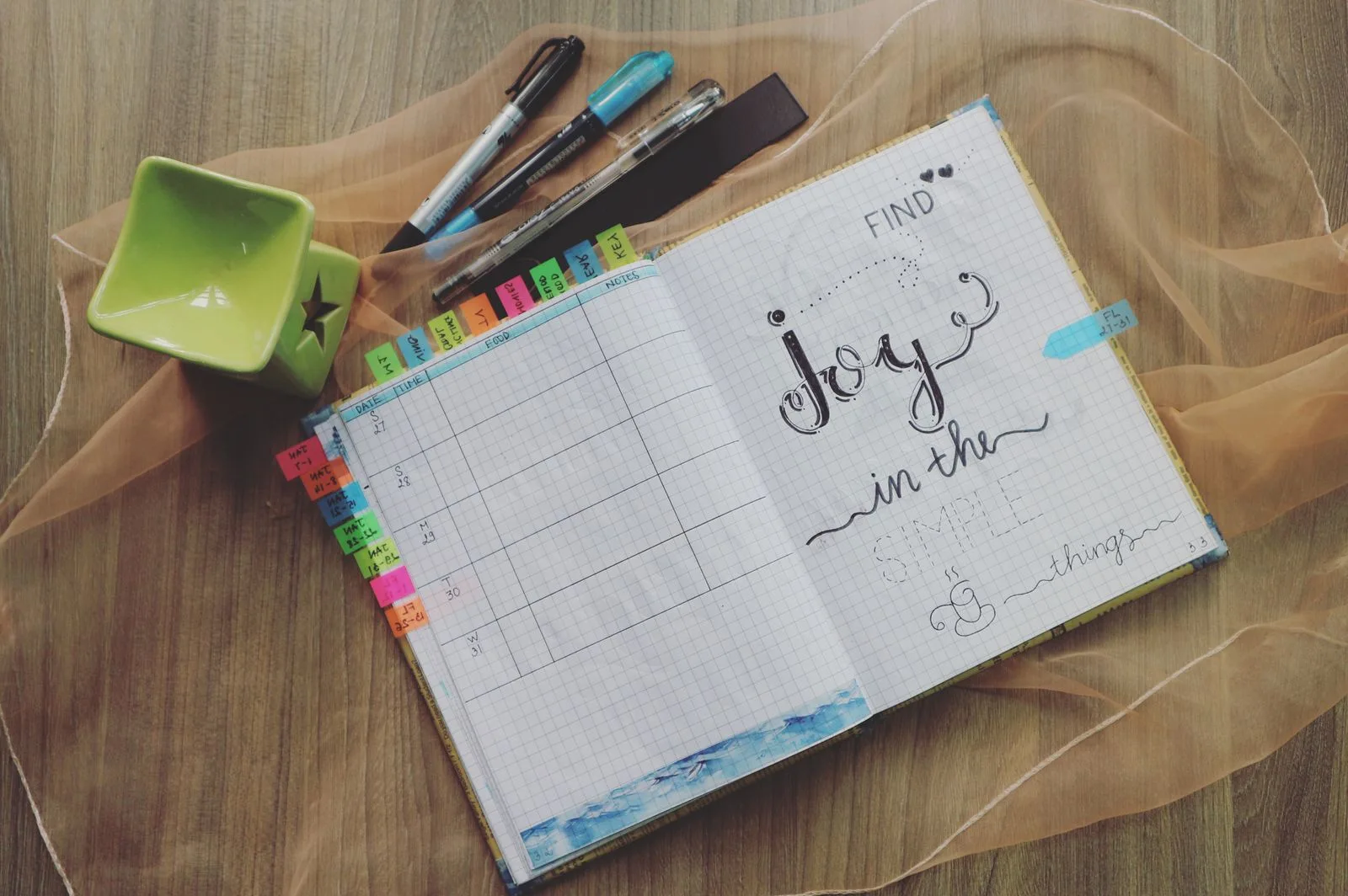 An open planner with pens on a wooden desk.