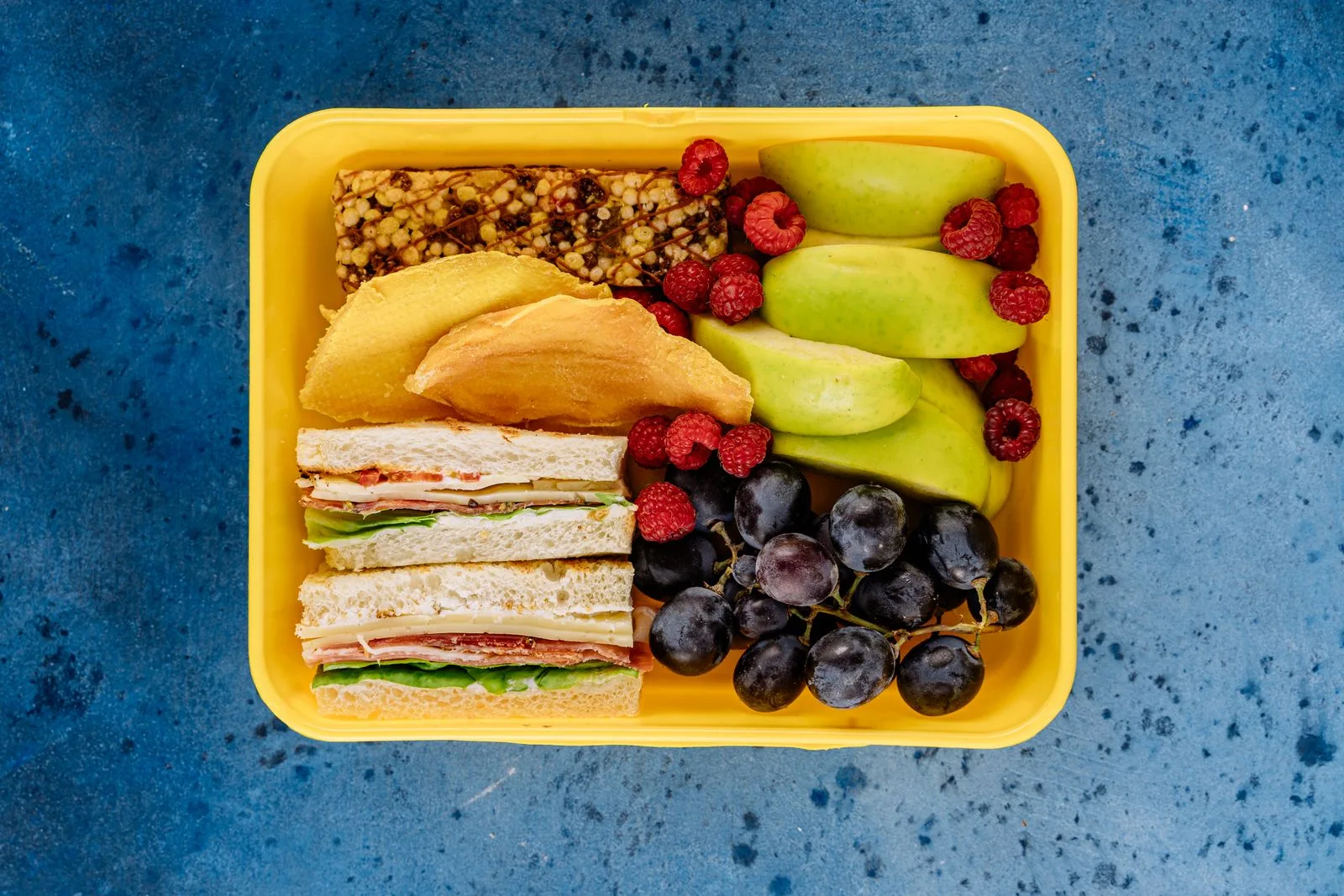 A yellow food container holding sandwiches and fruit.